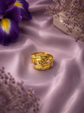 Gold leaf-wrap adjustable ring displayed on lavender satin fabric with purple floral accents.