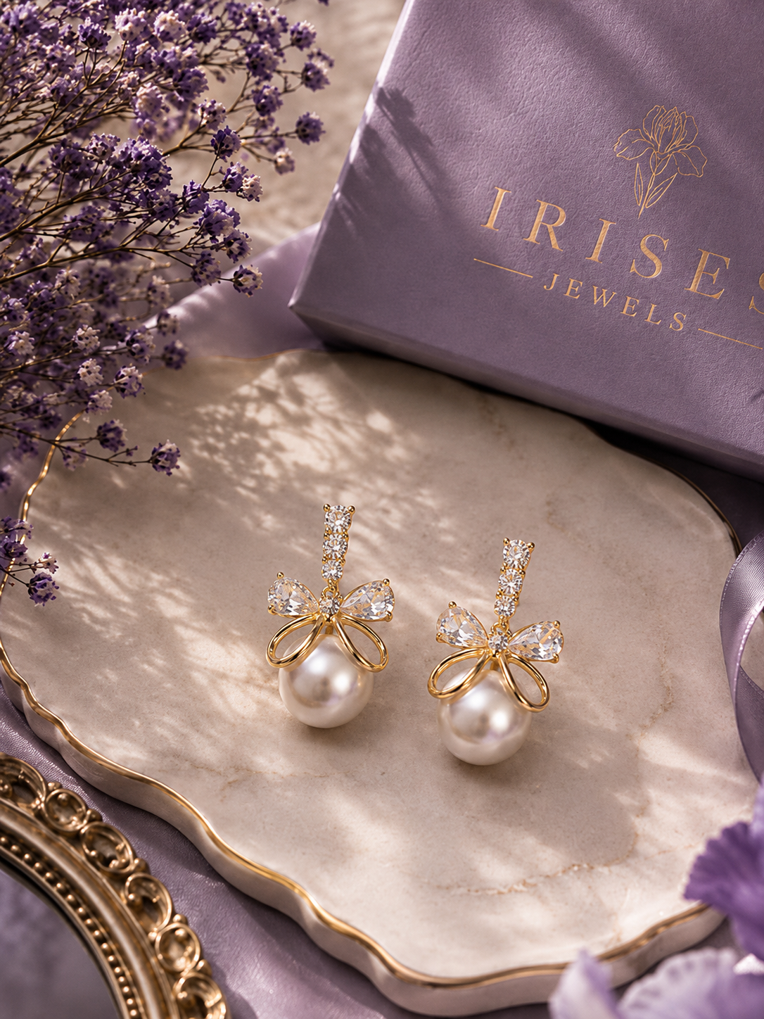 A Pearl Bow Crystal Drop Earrings featuring sparkling crystal bows with luminous faux pearl drops in a premium gold-tone finish with clear rhinestones and white pearl drops, displayed on a scalloped cream tray 