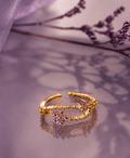 Gold adjustable floral ring with lavender crystal stones displayed on a soft purple reflective surface