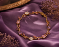 Gold floral bracelet with lavender, blush pink, and crystal stones arranged in a delicate tulip-inspired design on a beige marble surface.